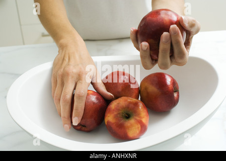 Donna mettendo le mele in coppa di frutta, vista ritagliata delle mani Foto Stock