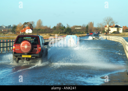 Le auto guidano in alta marea coprendo la strada sopraelevata che è l'unico collegamento stradale per la terraferma dell'Essex UK con l'isola di East e la città di West Mersea Foto Stock