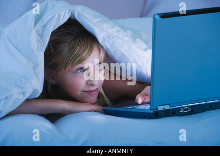 Ragazza adolescente sotto coperta guardando al laptop Foto Stock