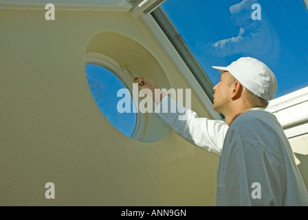 Pittore maschio si concentra sulla pittura finestra rotonda vicino al tetto in vetro Foto Stock