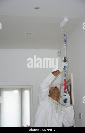 Pittore maschio si concentra sul soffitto dipinto in bianco Foto Stock