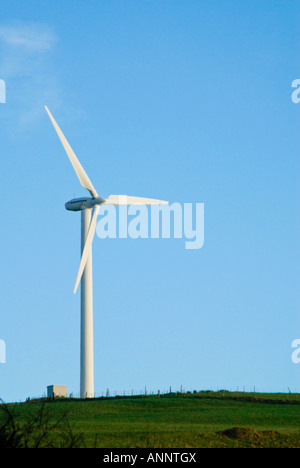 Vista verticale di comune tre pale della turbina eolica arroccato su una collina in una fattoria eolica contro un luminoso cielo blu Foto Stock