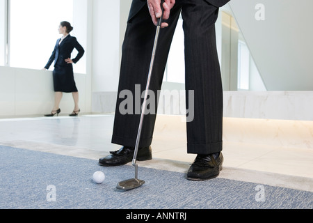 Vista di imprenditore per giocare a golf con la donna in piedi in background. Foto Stock