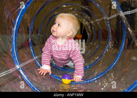 Ritratto orizzontale di un grazioso Caucasian Baby girl strisciando attraverso un vedere attraverso il tubo di plastica a un bambino piccolo gruppo Foto Stock