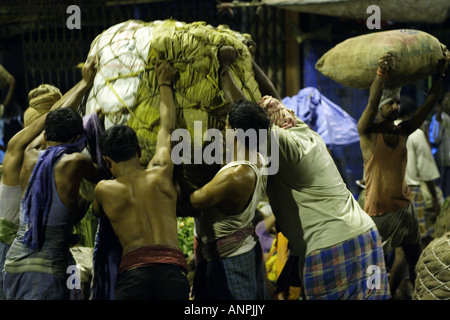 Gli uomini sollevare un carico pesante al mercato all'ingrosso di frutta e verdura in Kolkata, India. Foto Stock