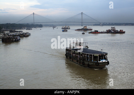 Una barca che porta i turisti in un viaggio lungo il Fiume Hooghly. Il Vidyasagar Seta sospensione ponte sospeso in background. Foto Stock