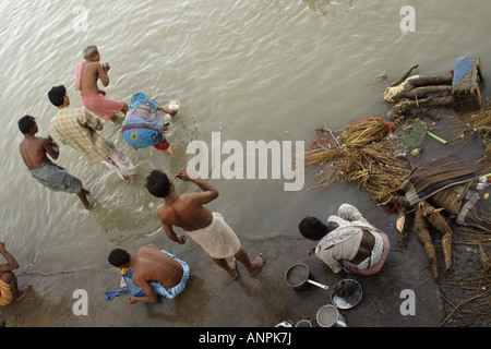 Una donna lava i suoi utensili da cucina nel Fiume Hooghly, in Kolkata, India. Accanto al suo stand chi wash. Foto Stock