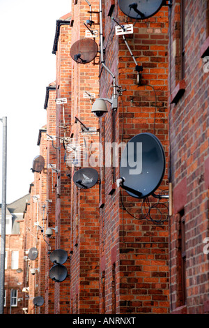 Una miriade di antenne paraboliche per la ricezione satellitare e le videocamere di sorveglianza fissato al lato del blocco casamento in Barrow-in-Furness, Cumbria, Inghilterra Foto Stock