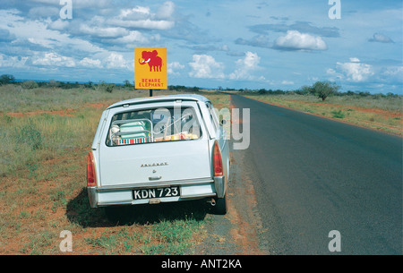 Peugeot 404 station wagon parcheggiata sul principale di Nairobi Mombasa road accanto a un cartello stradale la lettura ATTENZIONE ELEPHANT Kenya Africa orientale Foto Stock