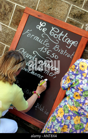 Donna menu scrittura sulla lavagna fuori del ristorante a Dinan Bretagna Francia Foto Stock