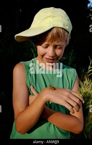 Il ragazzo, undici anni, tenendo un grasshopper sulla sua mano Foto Stock