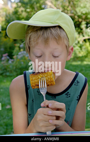 Il ragazzo, undici anni, è mangiare fritto o grigliato del mais con cunsumption Foto Stock