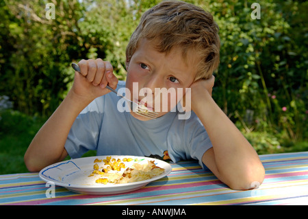 Il ragazzo, a nove anni. È sognante di mangiare il suo pranzo con mais Foto Stock