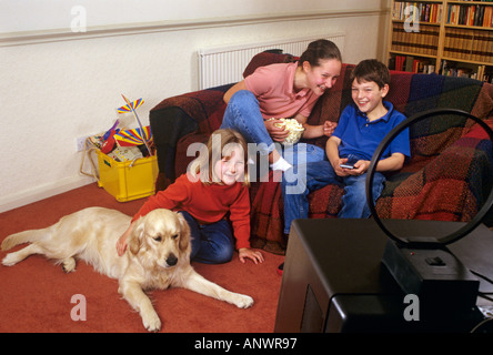 Due sorelle e il loro fratello felicemente guardando la piccola TV portatile a casa loro sala giochi con la famiglia cane Foto Stock