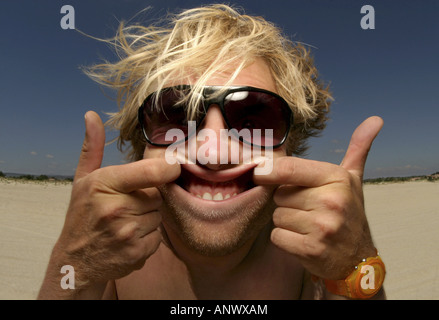 Crazy biondo Uomo con occhiali da sole rendendo un grimace in spiaggia Foto Stock