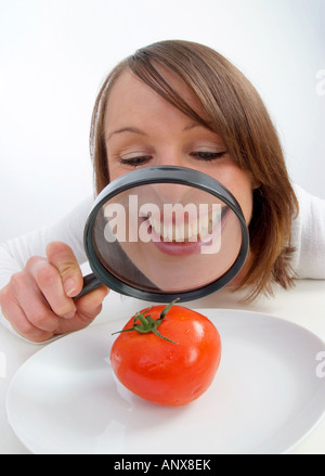 Giovane donna con lente di ingrandimento visto il pomodoro in corrispondenza della piastra Foto Stock