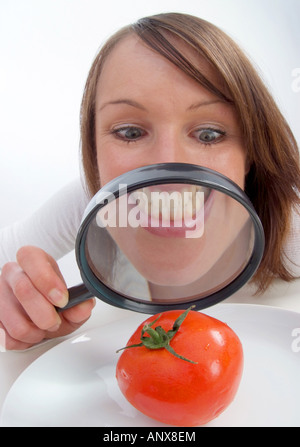 Giovane donna con lente di ingrandimento visto il pomodoro in corrispondenza della piastra Foto Stock