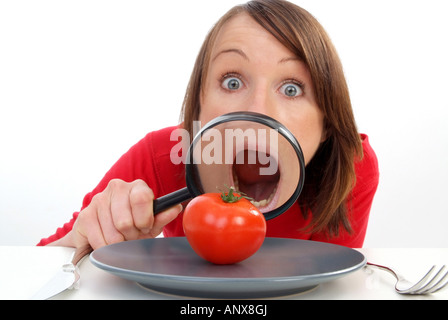 Giovane donna con lente di ingrandimento visto il pomodoro in corrispondenza della piastra Foto Stock