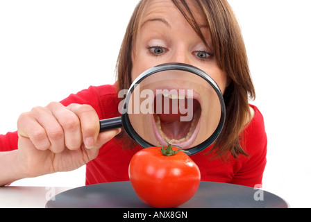 Giovane donna con lente di ingrandimento visto il pomodoro in corrispondenza della piastra Foto Stock