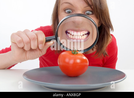 Giovane donna con lente di ingrandimento visto il pomodoro in corrispondenza della piastra Foto Stock