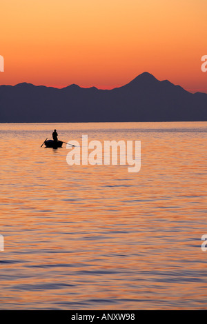 Silhouet di un pescatore solitario in piedi in una barca a remi la pesca Foto Stock