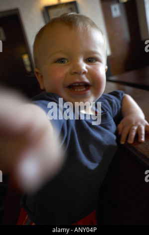 Un bambino di un anno ragazzo sorrisi come egli raggiunge la fotocamera Foto Stock