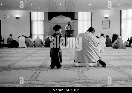 Un piccolo ragazzo sorge accanto tohis Padre pregando in Victor Street moschea, Manningham, Bradford, Yorkshire, Regno Unito Foto Stock