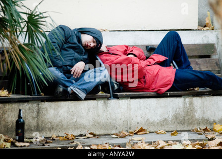 Giovani barboni di dormire su un banco di lavoro con una bottiglia di vino a Londra Foto Stock