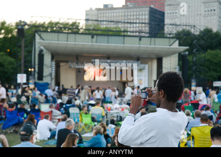 ILLINOIS Chicago folla di gente seduta in Grant Park Petrillo stadio all'aperto per il Jazz Festival uomo utilizzando una fotocamera digitale Foto Stock