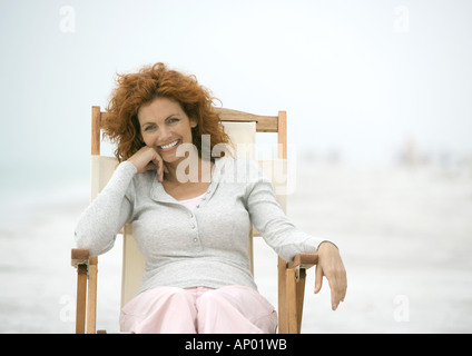 Donna seduta nella sedia spiaggia, sorridente Foto Stock