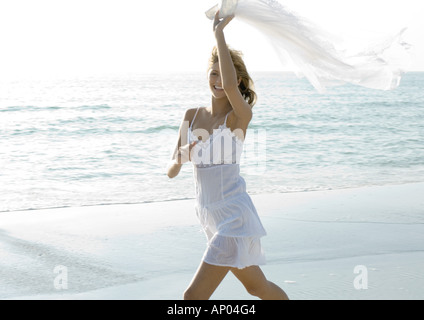 Donna sulla spiaggia, tenendo su pezzo di abbigliamento in vento Foto Stock
