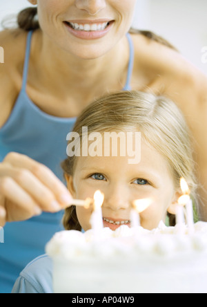 Madre accendendo candele sulla torta di compleanno per la ragazza Foto Stock