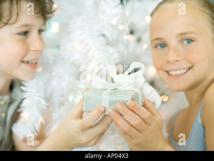 Ragazzo di consegnare la sorella dono nella parte anteriore dell albero di natale Foto Stock