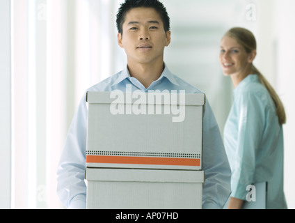Uomo che trasportava scatole in corridoio, femmina collega guardando Foto Stock