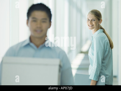 Uomo che trasportava scatole in corridoio, femmina collega guardando Foto Stock