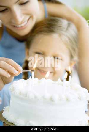 Madre accendendo candele sulla torta di compleanno per la figlia di Foto Stock