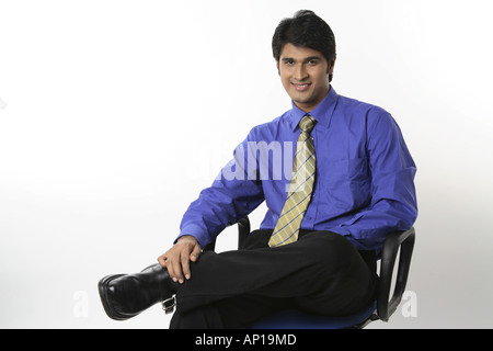 ANG200139 Executive seduti su una sedia sorridente indossando maglietta blu e Cravatta gialla felice modello di rilascio n. 687m Foto Stock