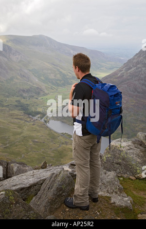 Giovane maschio walker guardando giù verso Llyn Ogwen nella valle dal monte Tryfan nel Parco Nazionale di Snowdonia North Wales UK Foto Stock