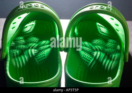 Una coppia di Bright Green Crocs zoccoli con luce che risplende attraverso il modello di fori della tomaia Foto Stock