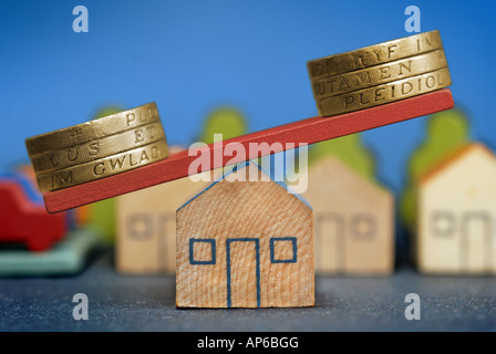 Un modello di casa con cancelletto monete bilanciato su di essa come un'altalena per illustrare il mercato degli alloggi e di decisioni di finanziamento. Foto Stock