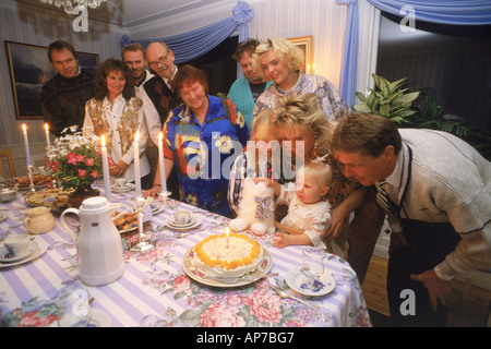 La prima festa di compleanno con tre generazioni della famiglia sorridente intorno al tavolo con la torta, candele e caffè Foto Stock