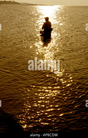 Silhouette del pescatore solitario guadare in golden acqua a Compo Beach, Westport, Connecticut all'alba. Foto Stock