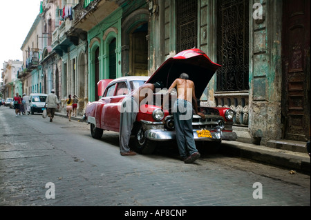 Classic American siede auto parcheggiate fuori vecchi edifici di l'Avana (Cuba) con due uomini di riparare il motore. Foto Stock
