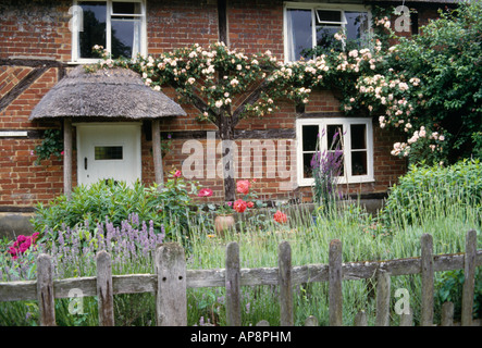 Post rustico+rail recinzione giardino di bordatura nella parte anteriore del mattone con travi di legno rustico con portico con tetto in paglia e rosa rosa rampicante Foto Stock