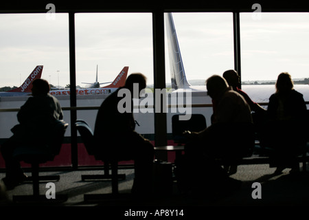 I passeggeri in attesa nella lounge nella parte anteriore della finestra a Belfast International Airport Irlanda del Nord Foto Stock