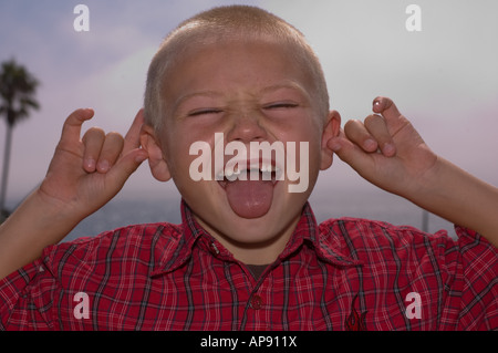 Parte anteriore denti mancanti Ragazzo che sorride con la lingua fuori tirando le orecchie Foto Stock