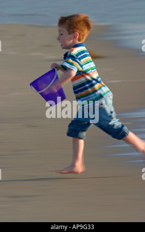Un ragazzino gare dall'acqua entrante mentre presso la spiaggia. Foto Stock
