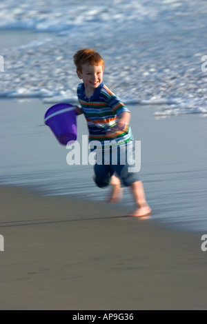 Un attraente giovane ragazzo viene eseguito dalle onde durante il gioco in spiaggia. Foto Stock