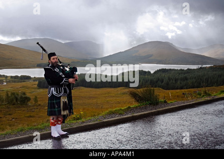 Piper in highland dress giocando sul ciglio della strada si affaccia su loch Tulla kilt in tartan sporran cornamuse scena della montagna Foto Stock