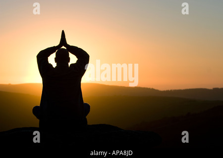 Profilo di Silhouette di un orante seduto su una collina di sunrise Foto Stock